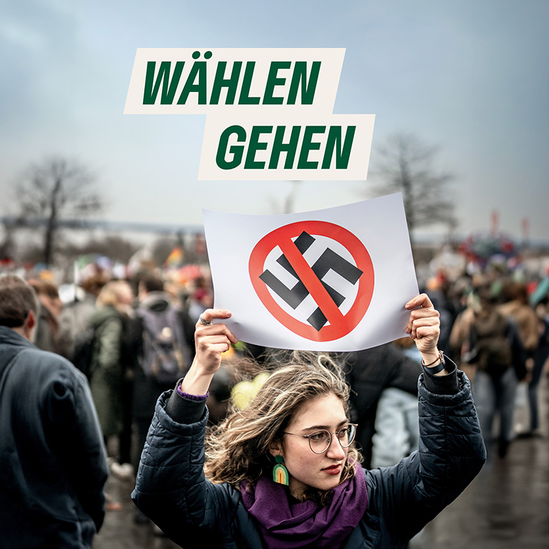 Frau mit Poster in der Hand: Aufdruck ist ein durchgestrichenes Hakenkreuz